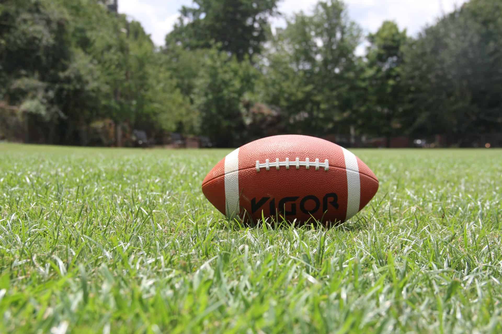 A football is laying on the grass in front of trees.