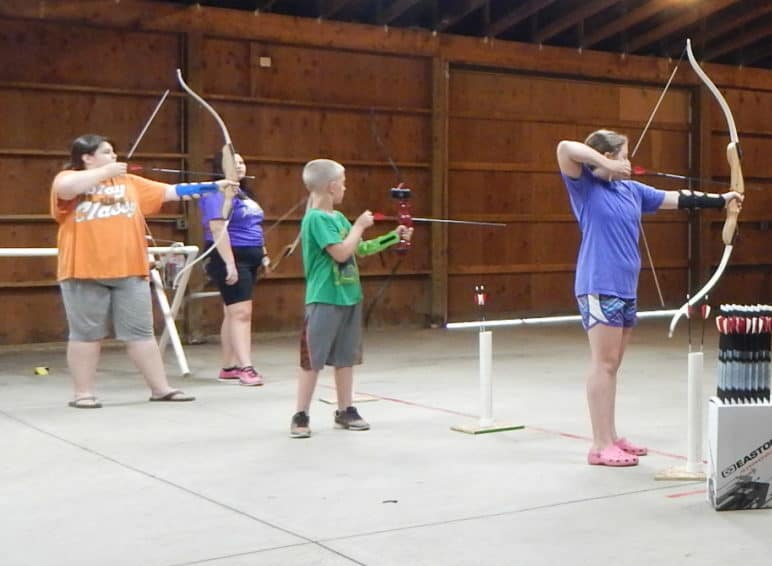 A group of people practicing archery in a barn.