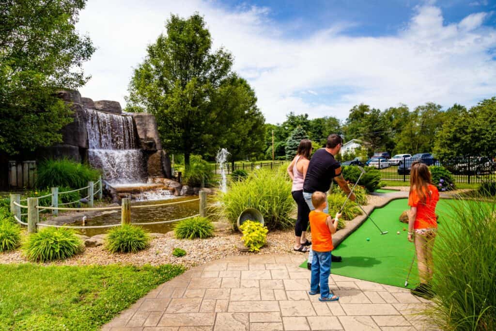 A family is playing mini golf near a waterfall.