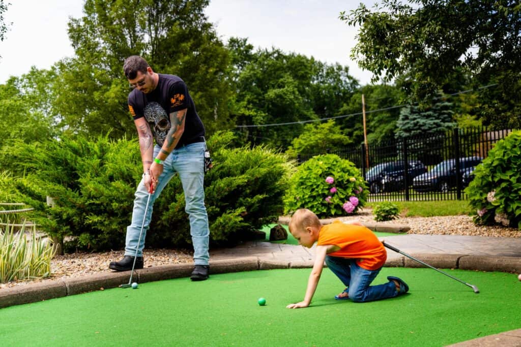 A man and a child playing mini golf at a park.