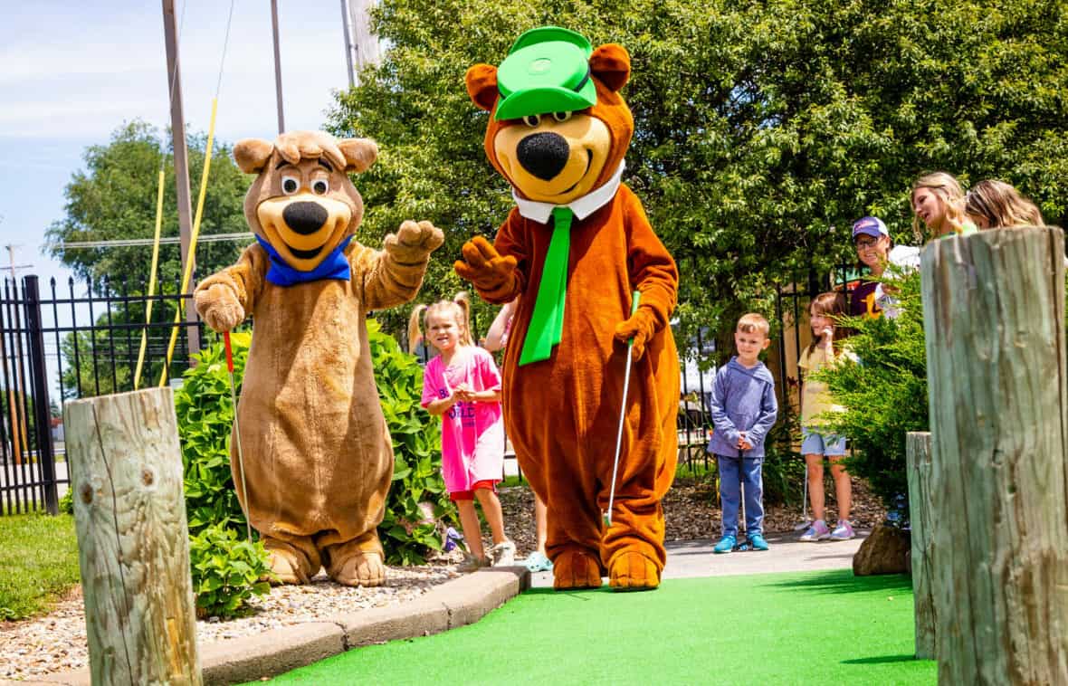 A group of children and mascots on a mini golf course.