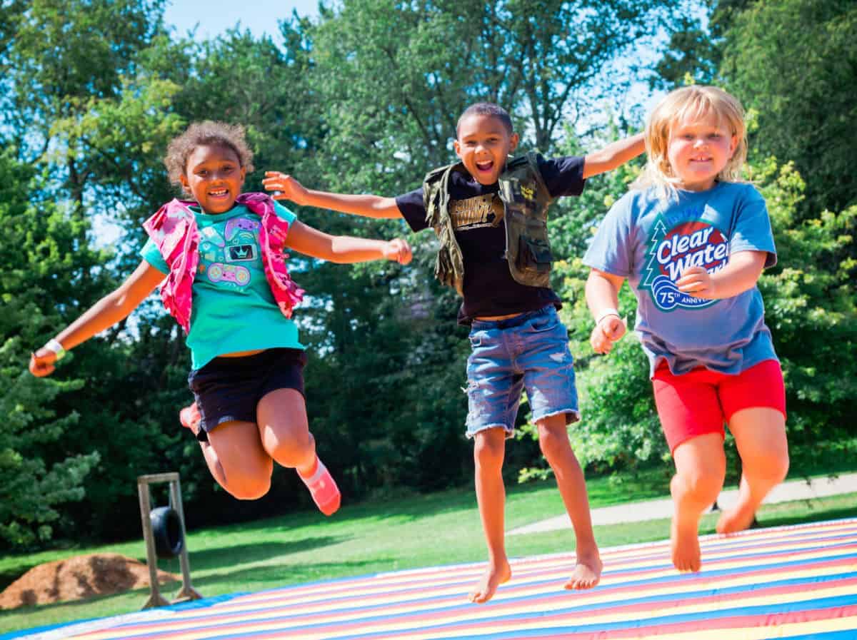 Three children jumping on a trampoline in a park.