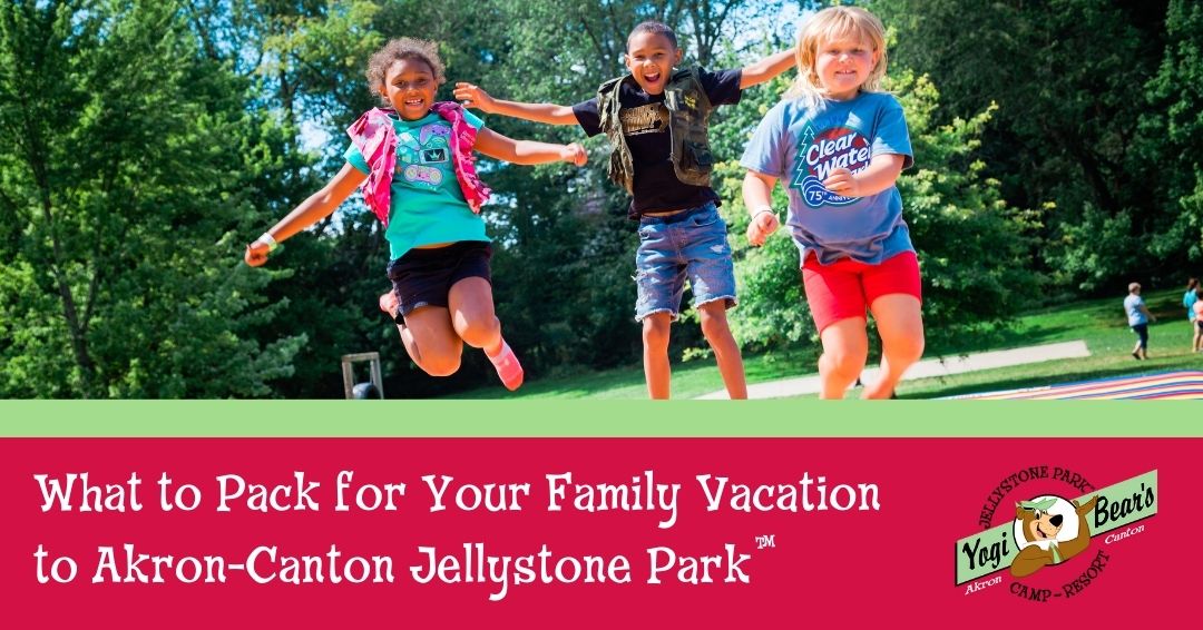 Three children are jumping and smiling outdoors on a sunny day. Text below reads: “What to Pack for Your Family Vacation to Akron-Canton Jellystone Park.”.
