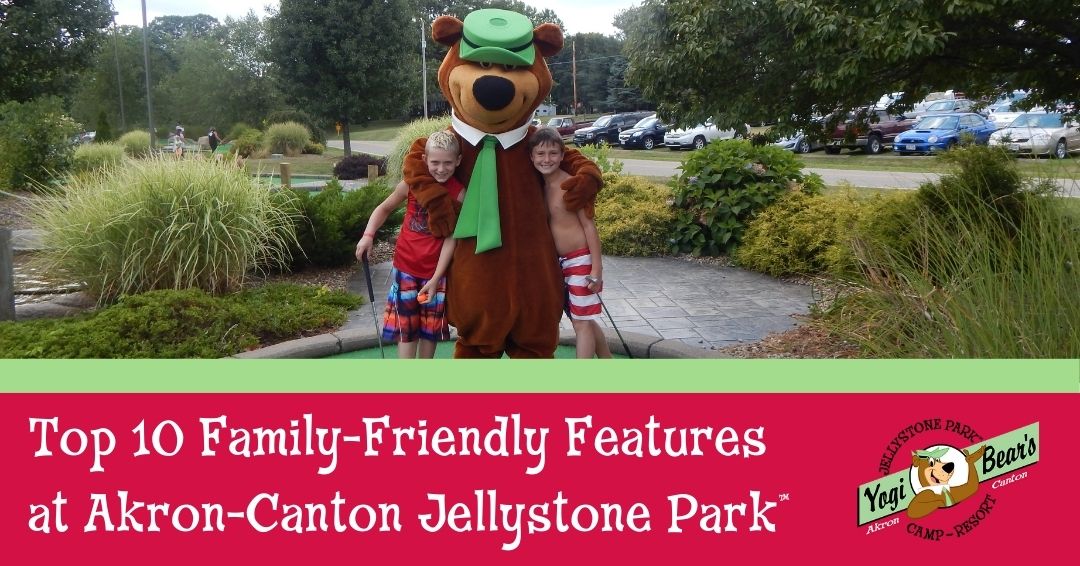 Two children in swimsuits stand beside a person in a Yogi Bear costume at a mini-golf course, with trees and cars visible in the background.