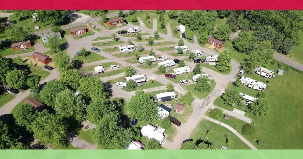 Aerial view of an RV park with several campers, cabins, and trees arranged along winding roads on a sunny day.