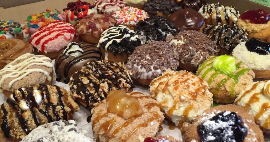 An assortment of decorated donuts with various colorful frostings, toppings, and drizzles arranged closely together in a box.