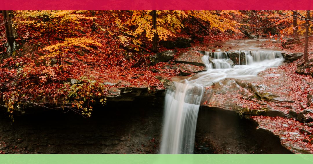 A waterfall flows over rocks surrounded by trees with vibrant autumn foliage; the image has red and green borders at the top and bottom.