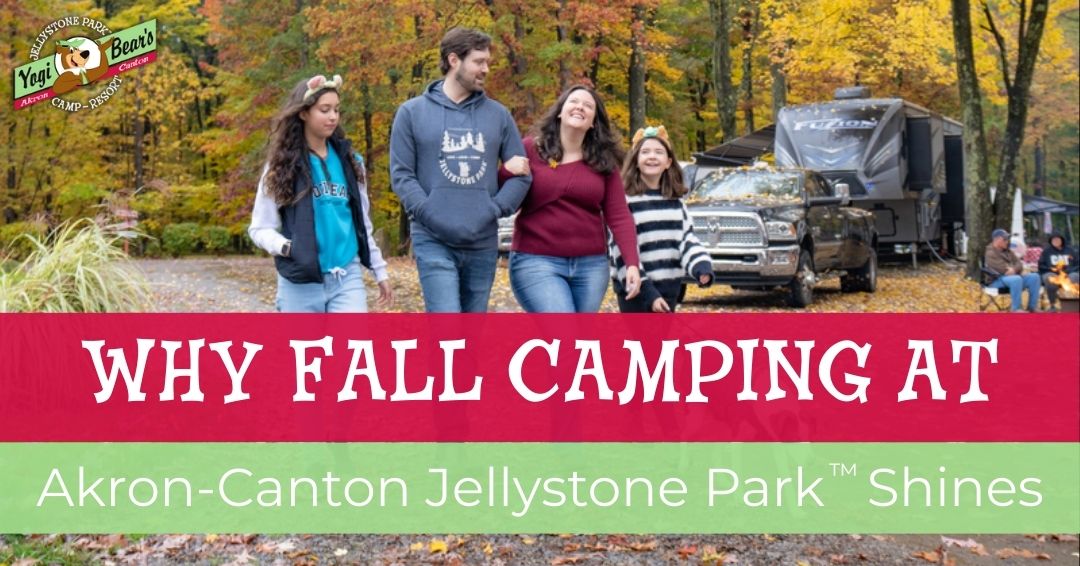 A family of four walks together at a campsite with an RV and autumn trees in the background. Text reads: “Why fall camping at Akron-Canton Jellystone Park™ shines.”.