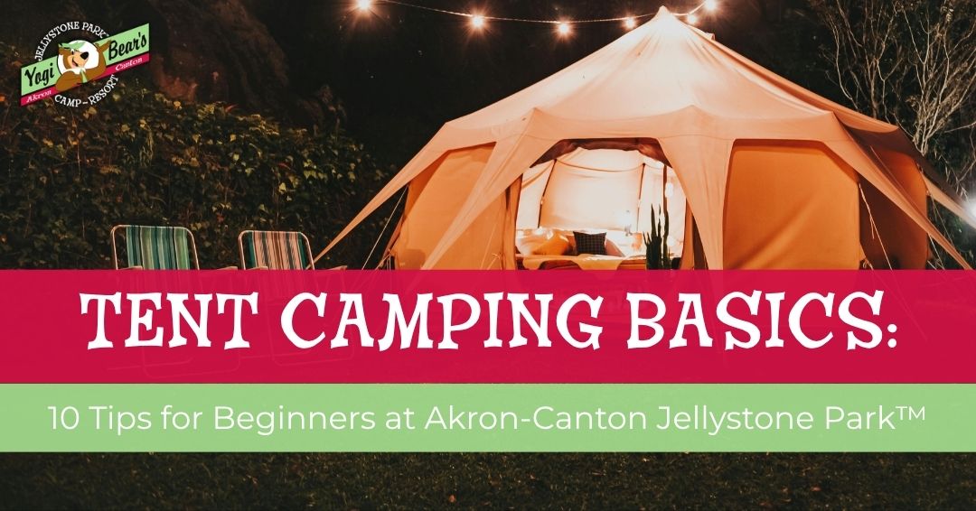 A lit canvas tent at night with two empty chairs outside; text reads "Tent Camping Basics: 10 Tips for Beginners at Akron-Canton Jellystone Park™.