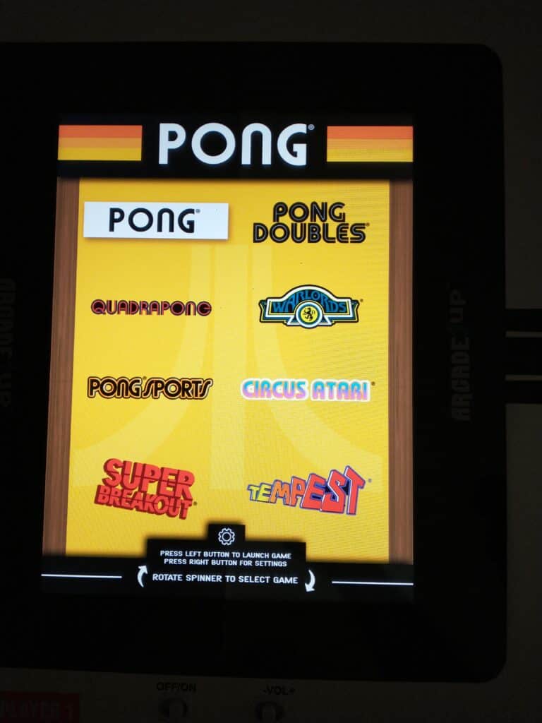 An arcade game screen displays a menu with game options: Pong, Pong Doubles, Quadrapong, Warlords, Pong Sports, Circus Atari, Super Breakout, and Tempest.