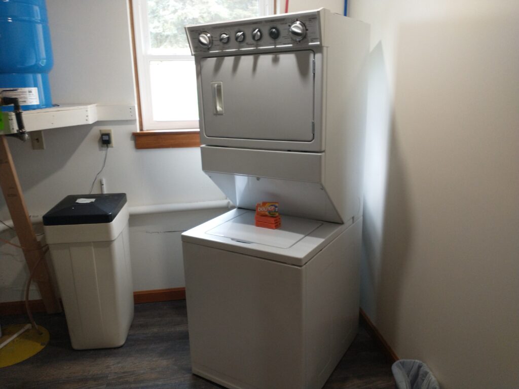 A stacked washer and dryer unit in a laundry room with a box of detergent on top of the washing machine.