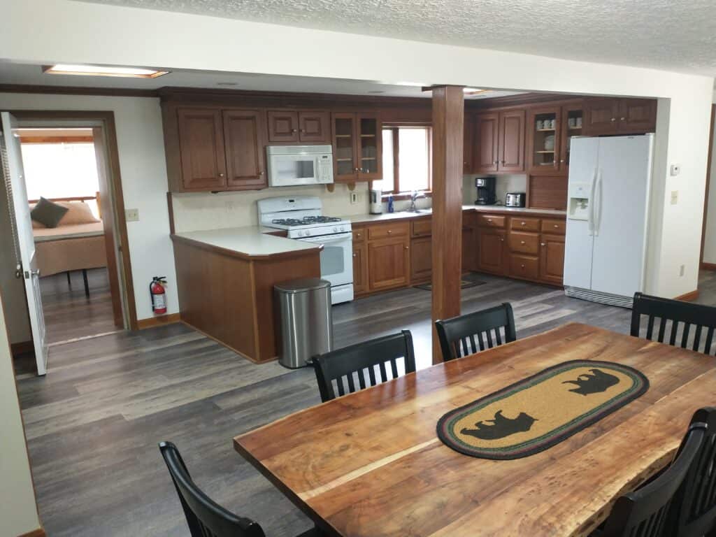 Spacious kitchen with wooden cabinets, white appliances, and a dining table with a bear-themed runner in the foreground.
