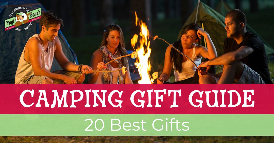 Four people sit around a campfire at night roasting marshmallows, with tents in the background. Text overlay reads “Camping Gift Guide: 20 Best Gifts.”.