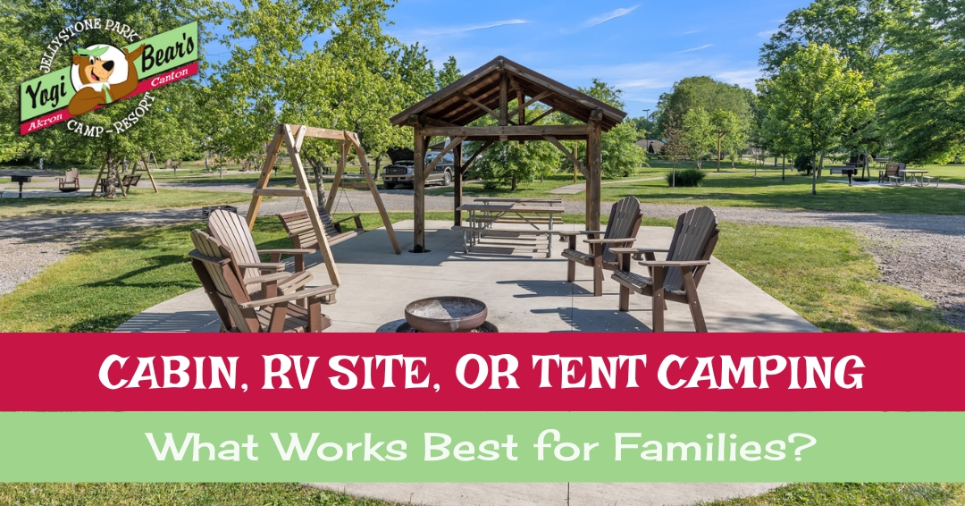 Outdoor campsite with wooden chairs, a picnic table, and a fire pit under a wooden shelter; sign promotes cabin, RV, or tent camping options for families at Yogi Bear’s Jellystone Park.