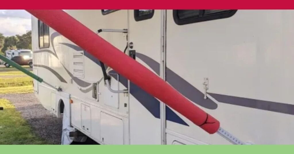 Red and green pool noodles are attached to the awning arms of a white RV parked on grass, with a gray and blue graphic on its side.