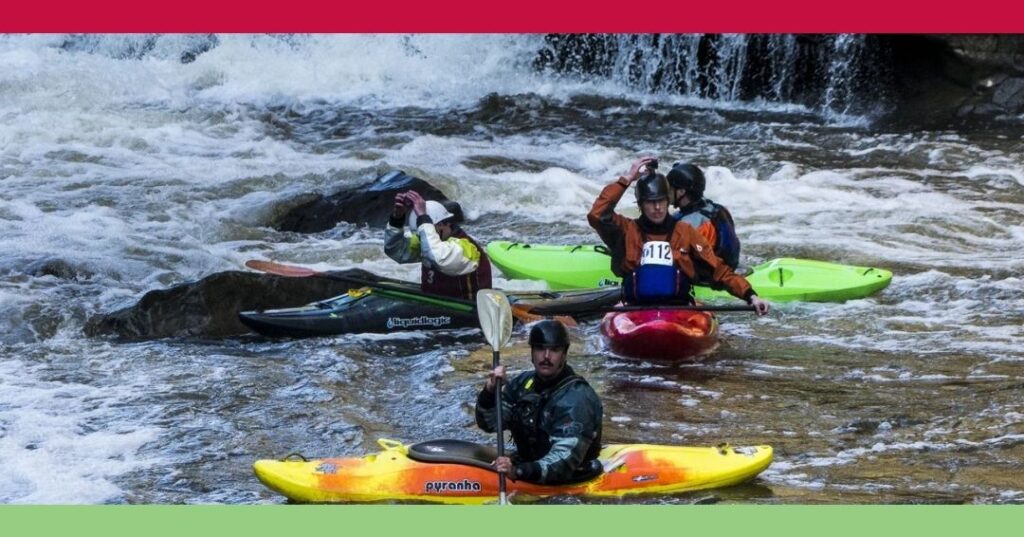 Four people in kayaks paddle in a river with whitewater rapids; three are close together while one is in the foreground facing the camera.