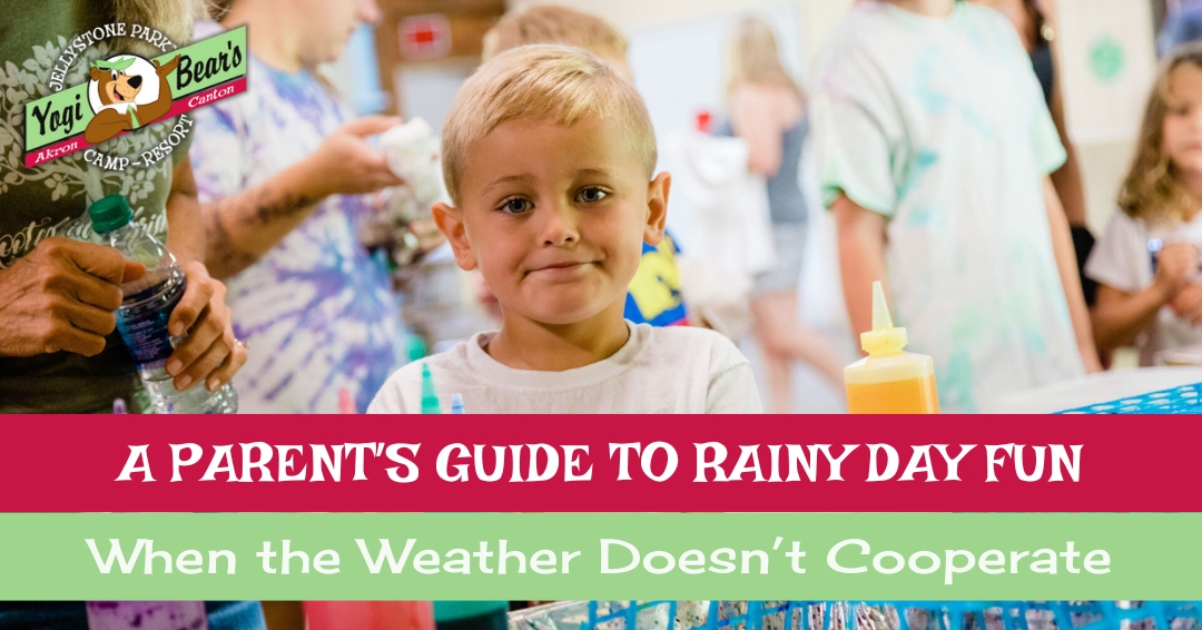 A young boy stands indoors at a table with bottles of colored liquid, surrounded by other children, during a rainy day activity at camp.